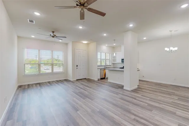an empty room with wooden floor a ceiling fan and kitchen view