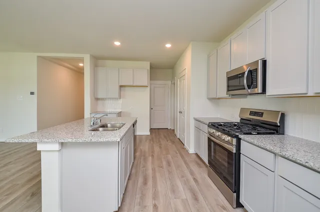 a kitchen with stainless steel appliances granite countertop a stove a sink and a microwave