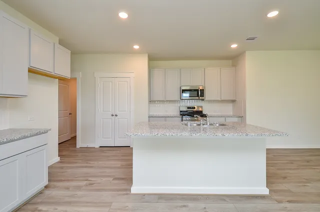 a view of a kitchen with kitchen island a sink wooden floor and stainless steel appliances