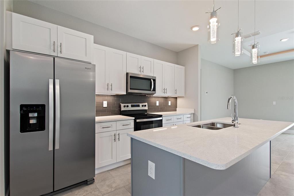24399 Southwest Kingsway Circle Punta Gorda, FL 33983 - Photo 15 of 38 a kitchen that has a refrigerator a stove a microwave and white cabinets with wooden floor