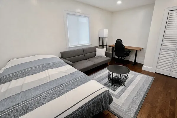 a bedroom with a bed a couch and wooden floor