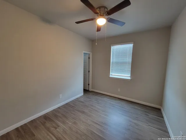 an empty room with wooden floor chandelier fan and windows