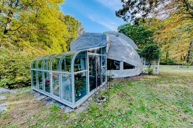 a view of house with large trees and flower plants in front of main door