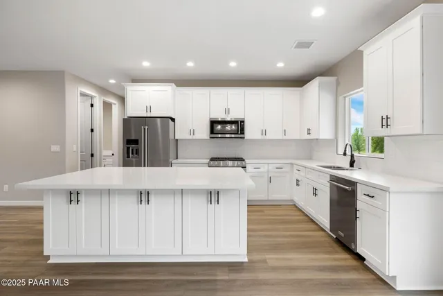 a kitchen with stainless steel appliances kitchen island granite countertop a stove a sink a refrigerator and white cabinets