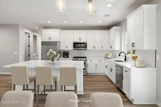 a kitchen that has a lot of white cabinets and stainless steel appliances
