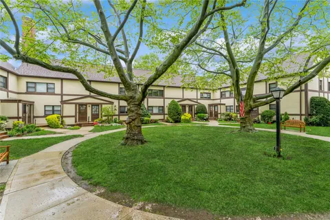 a view of a white house in front of a big yard with large trees