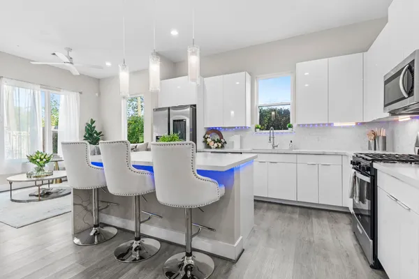 a kitchen with stainless steel appliances kitchen island granite countertop a stove a sink a refrigerator white cabinets and wooden floor