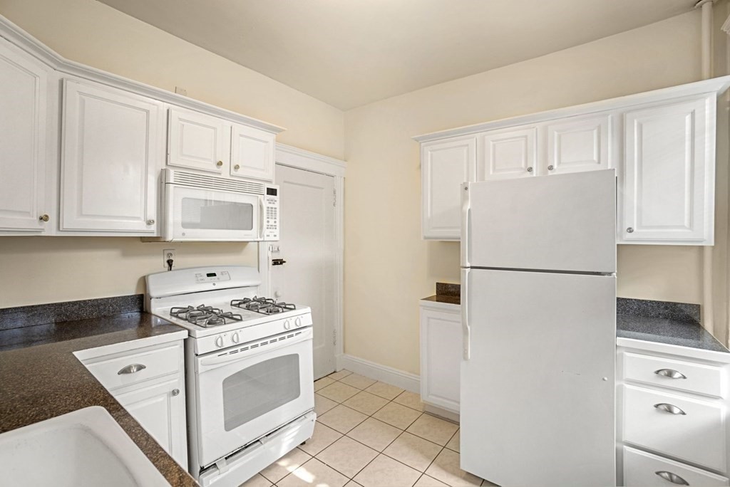 a white refrigerator freezer and a stove sitting inside of a kitchen with cabinets
