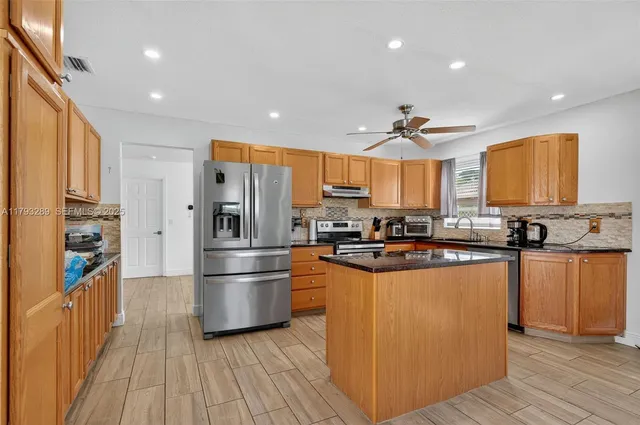 a kitchen with stainless steel appliances a dining table chairs refrigerator and sink
