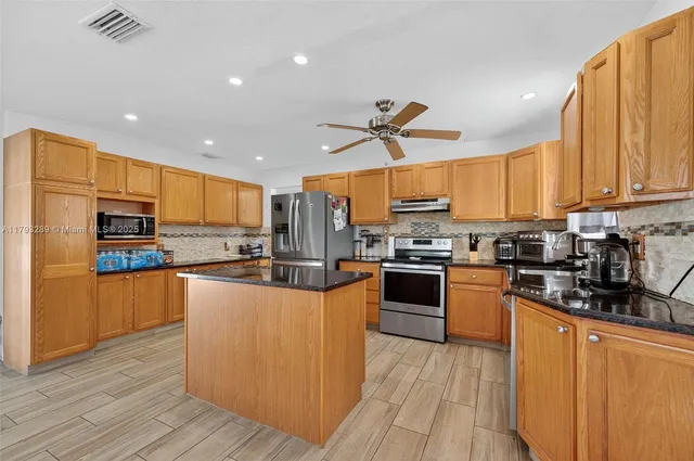 a kitchen with stainless steel appliances a dining table chairs refrigerator and sink