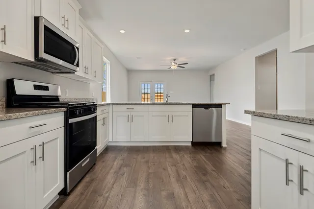 a kitchen with stainless steel appliances kitchen island granite countertop a stove top oven a sink and white cabinets