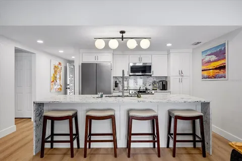 a kitchen with stainless steel appliances granite countertop a dining table chairs refrigerator and microwave