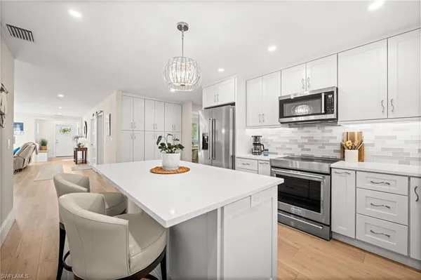 a kitchen with stainless steel appliances kitchen island granite countertop a stove a sink a microwave a refrigerator and white cabinets