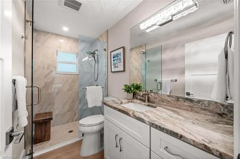 a bathroom with a granite countertop sink a toilet a mirror and shower