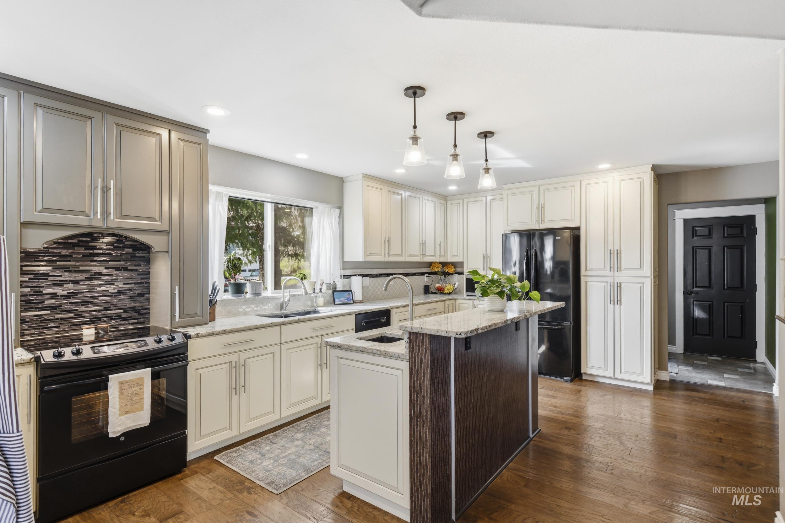 301 State Street Juliaetta, ID 83535 - Photo 16 of 41 Kitchen with black appliances, light stone counters, dark wood-style floors, hanging light fixtures, and a center island with sink