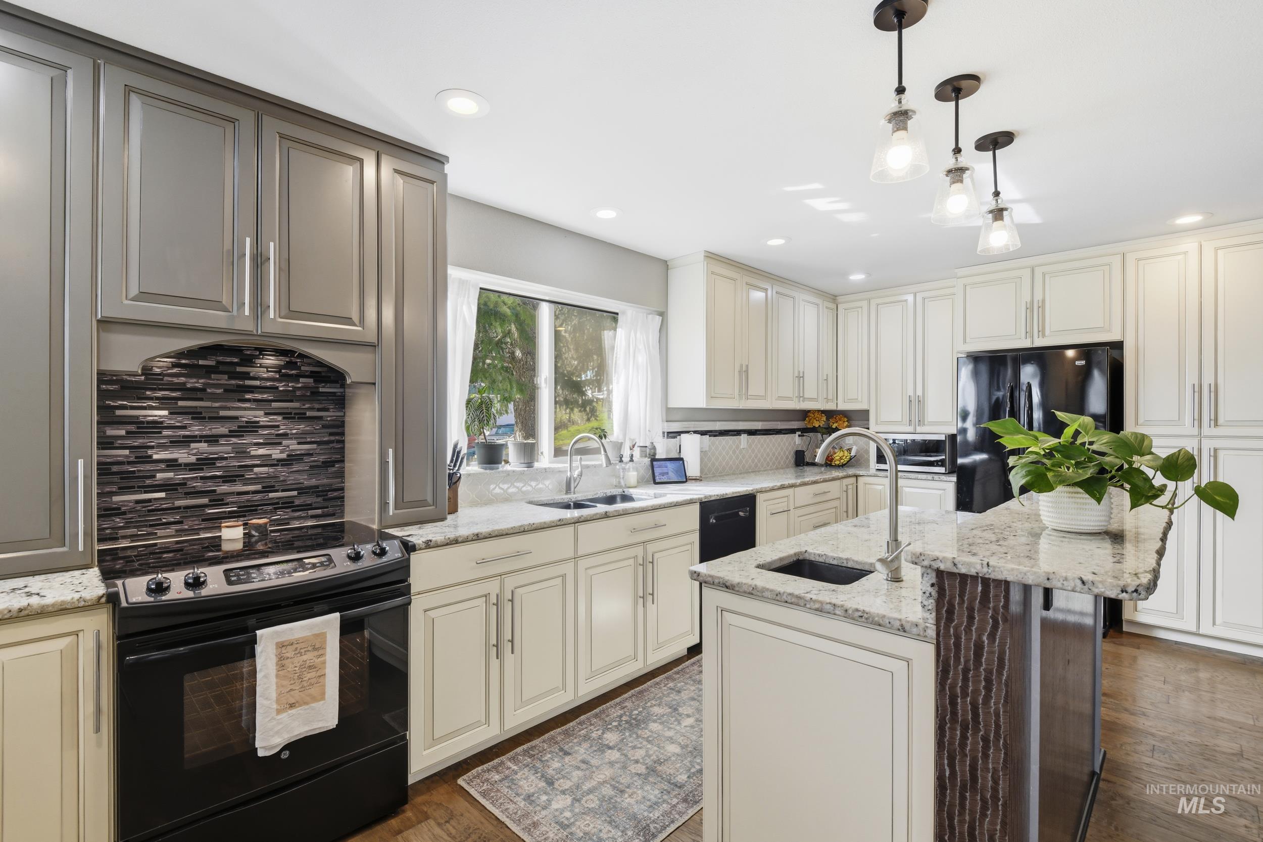 301 State Street Juliaetta, ID 83535 - Photo 19 of 41 Kitchen with cream cabinetry, black appliances, decorative light fixtures, light stone countertops, and a center island with sink