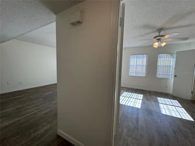 a view of an empty room with wooden floor and fan