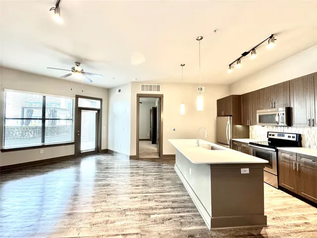 a large kitchen with stainless steel appliances kitchen island a stove a refrigerator a sink dishwasher with a dining table and chairs with wooden floor