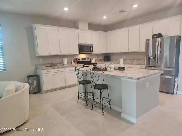 a kitchen with stainless steel appliances granite countertop a table chairs sink refrigerator and cabinets