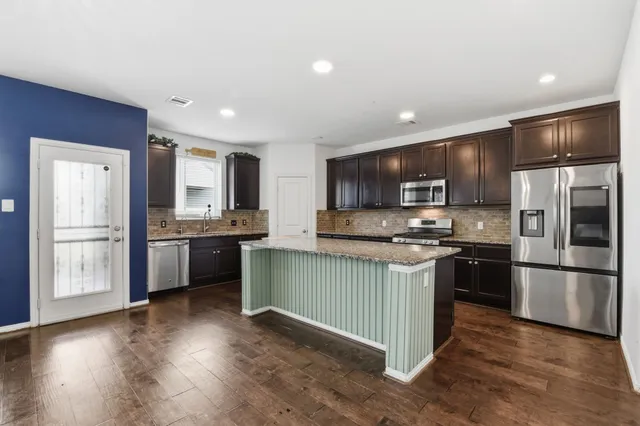 a kitchen with stainless steel appliances kitchen island granite countertop a refrigerator stove top oven and sink