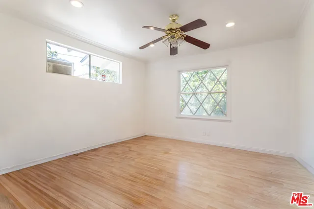 an empty room with wooden floor chandelier fan and windows