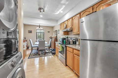 a kitchen with stainless steel appliances granite countertop a refrigerator a sink dishwasher a stove and a dining table with wooden floor