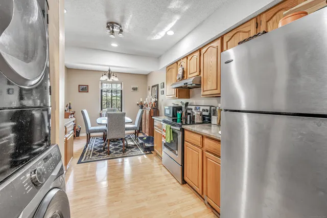 a kitchen with stainless steel appliances granite countertop a refrigerator a sink dishwasher a stove and a dining table with wooden floor