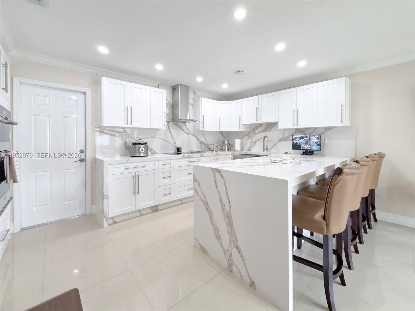 a kitchen with stainless steel appliances kitchen island granite countertop a sink a stove a refrigerator with white cabinets and wooden floor