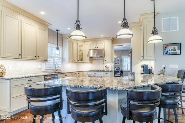 a kitchen with stainless steel appliances kitchen island granite countertop a refrigerator a stove and white cabinets with wooden floor