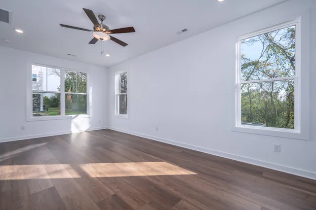 an empty room with wooden floor fan and windows