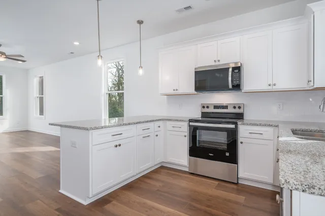 a kitchen with stainless steel appliances white cabinets a sink a stove a microwave and wooden floors