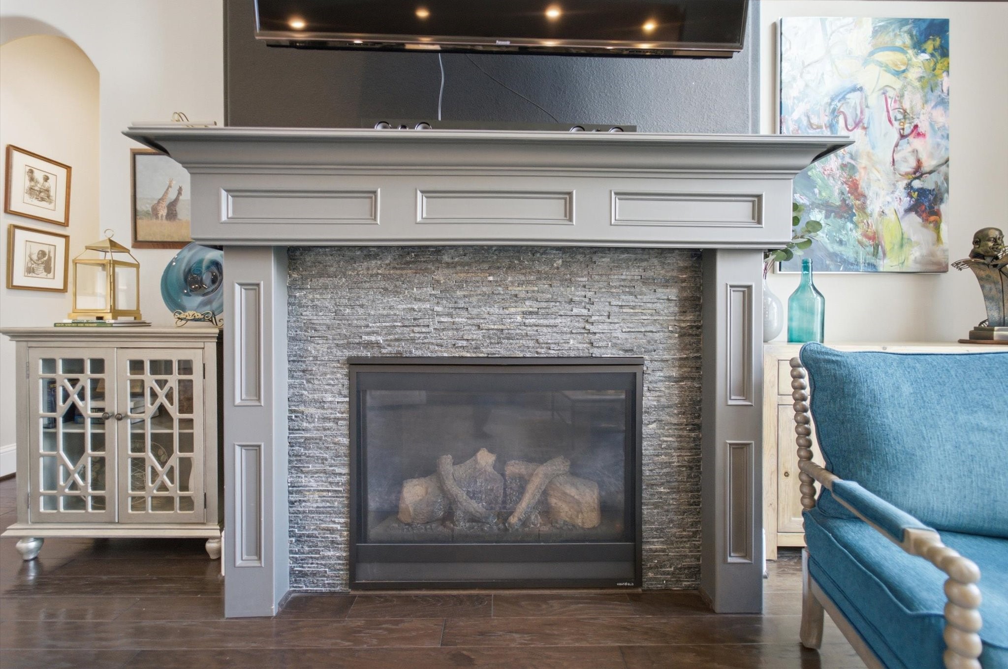 23722 Thortons Park Lane Spring, TX 77389 - Photo 31 of 48 Elegant living room with a stylish fireplace featuring a stone surround and a gray mantel. The space is tastefully decorated with art pieces, a blue armchair, and a chic cabinet, creating a cozy and inviting atmosphere.