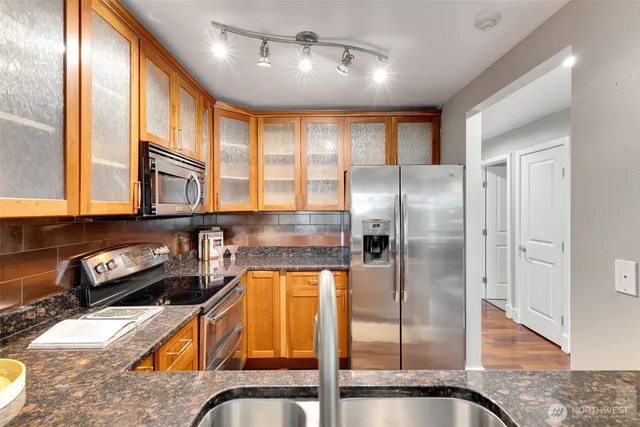 a kitchen with stainless steel appliances granite countertop a refrigerator a stove and a sink with wooden floor