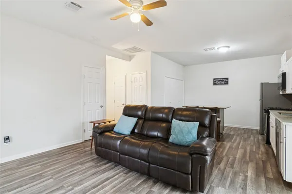 a kitchen with a stove a sink white cabinets and chairs with wooden floor