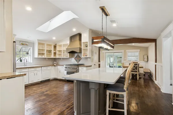 a kitchen with stainless steel appliances granite countertop a stove a refrigerator a kitchen island a dining table and chairs with wooden floor