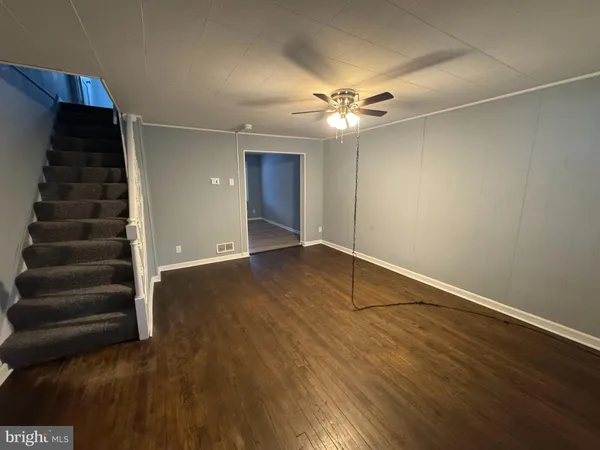 an empty room with wooden floor a ceiling fan and staircase