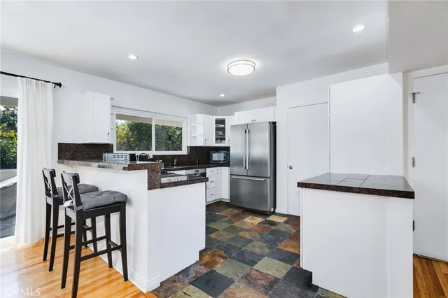 a kitchen with stainless steel appliances granite countertop a refrigerator a stove a sink a dining table and chairs with wooden floor