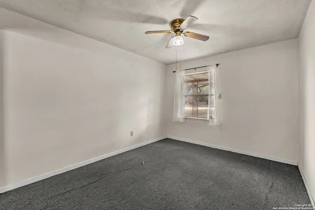 an empty room with a chandelier fan and windows