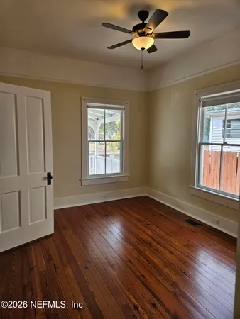 an empty room with wooden floor chandelier fan and windows