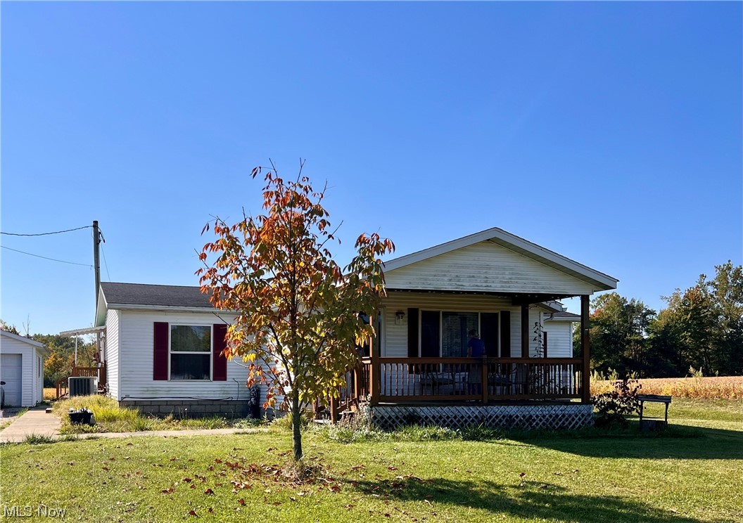 View of front of property featuring a front lawn, central air condition unit, a garage, and covered porch