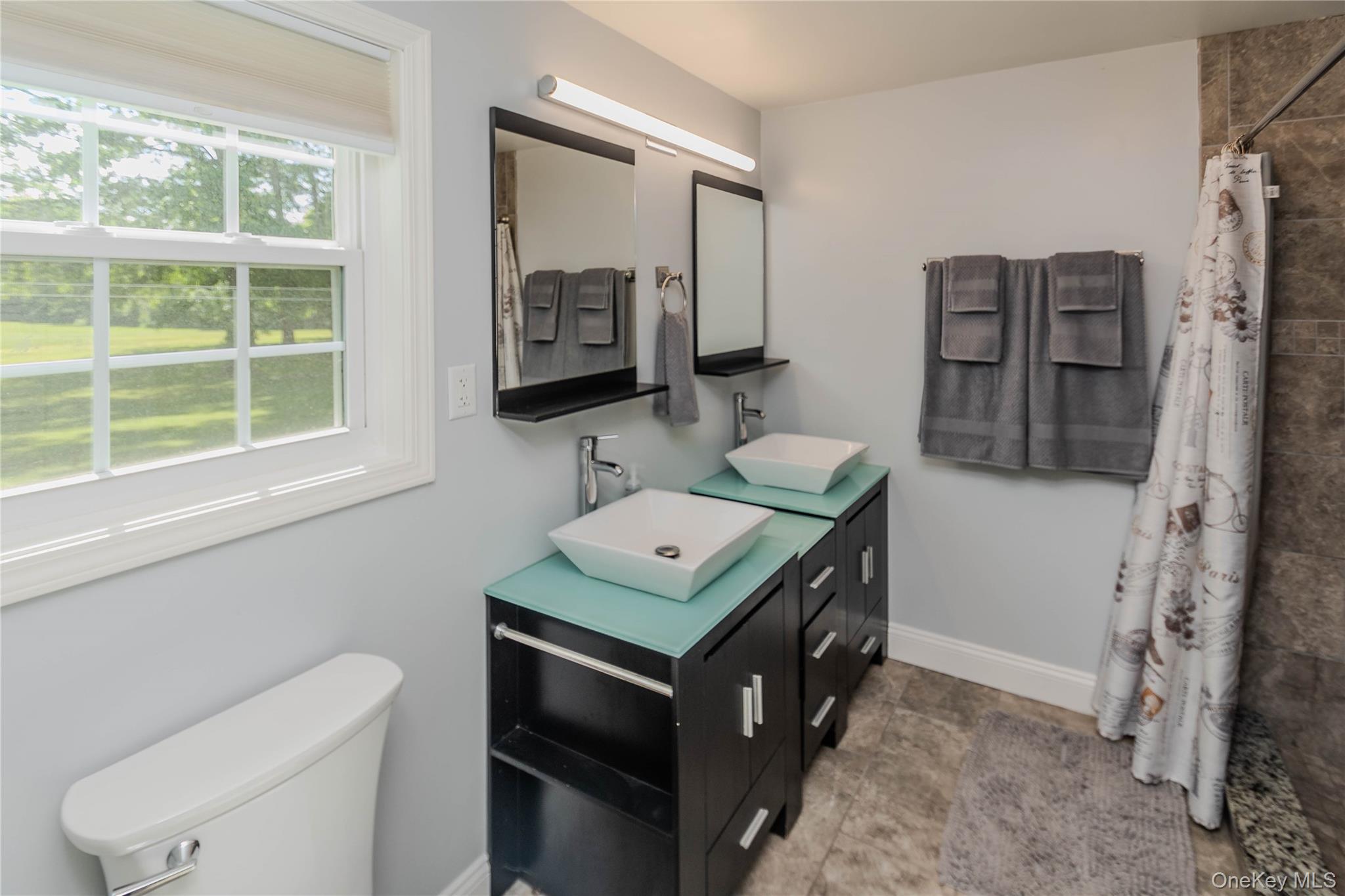 15 Van Dewark Road Middletown, NY 10941 - Photo 25 of 41 Dual vessel sinks with modern chrome fixtures atop dark wood-finish vanities, complemented by a tiled shower surround and a single-pane window