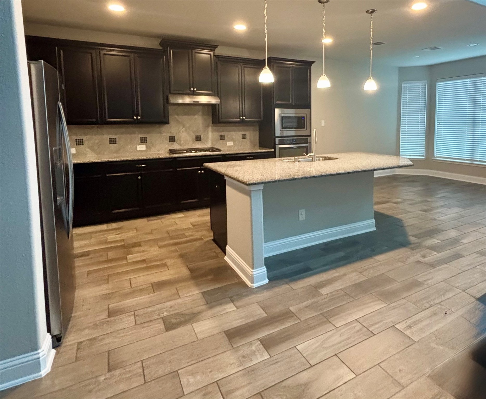 14915 Gyrfalcon Fork Cypress, TX 77429 - Photo 4 of 24 Chic kitchen featuring modern dark cabinets, sleek stainless steel appliances, and a spacious granite island, perfect for entertaining.
