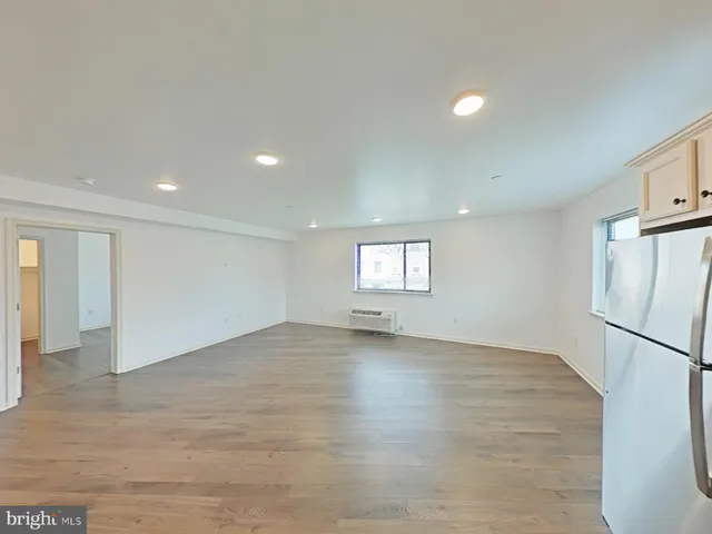 an empty room with wooden floor and a refrigerator