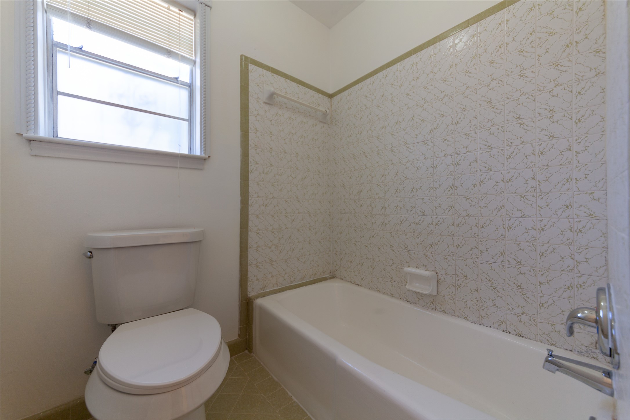 8826 Roos Road Houston, TX 77036 - Photo 27 of 42 This bathroom features a bathtub with patterned tile surround, a toilet, and a window for natural light. The space is clean and functional, with neutral tones.