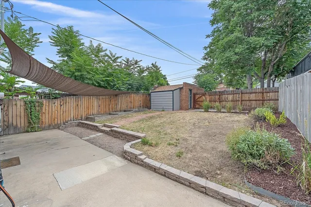 a backyard of a house with plants and trees with wooden fence