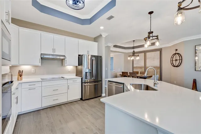 a kitchen with stainless steel appliances kitchen island granite countertop a refrigerator oven a sink dishwasher and white cabinets with wooden floor