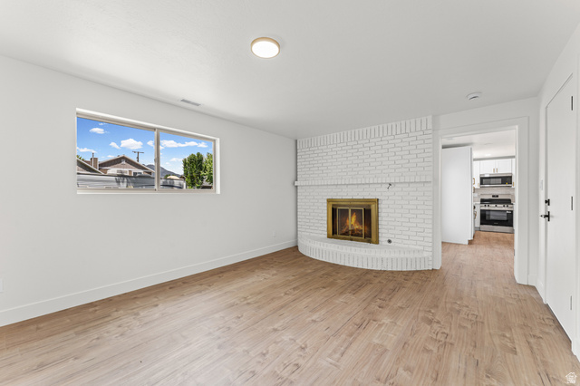 1898 West 600 South Provo, UT 84601 - Photo 26 of 32 Spacious interior featuring a white-painted brick fireplace with a brass-trimmed firebox, wood-finish flooring, and a large window with white trim