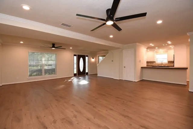 an empty room with wooden floor a ceiling fan and kitchen view