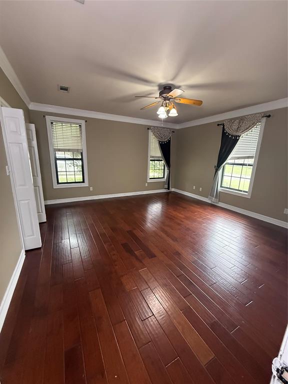 201 Woodhaven Drive Minden, LA 71055 - Photo 12 of 31 Spacious room featuring rich wood-finish flooring, neutral wall tones, multiple windows with blinds, a ceiling fan with integrated lighting, and white crown molding