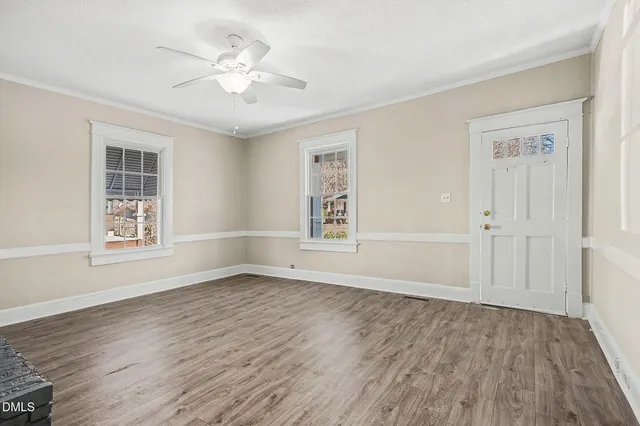 an empty room with wooden floor chandelier fan and windows